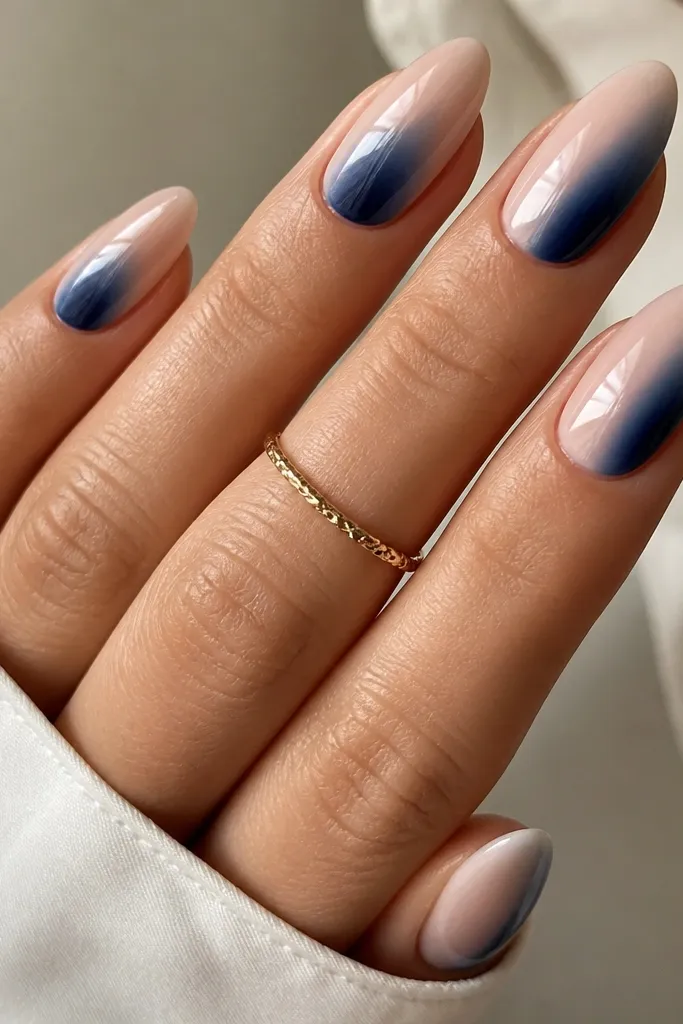 Almond nails with a nude base. A sapphire blue gradient runs from the sidewall toward the center at the mid-to-tip area, fading softly. Glossy top coat.