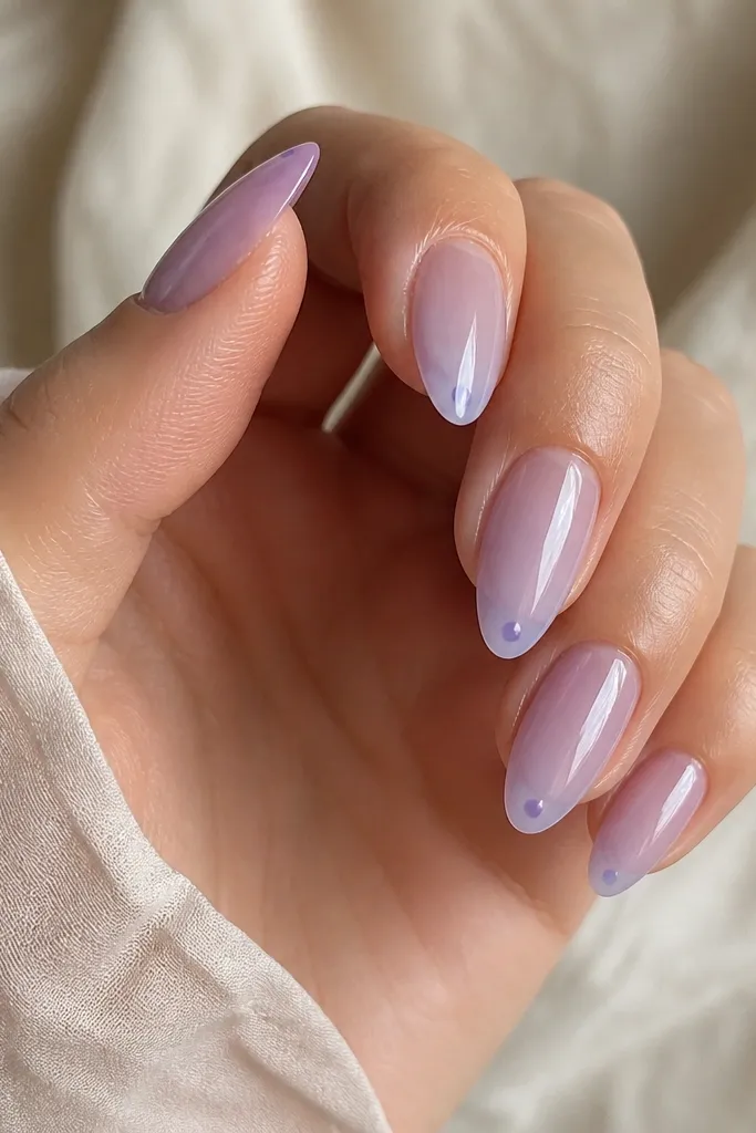Glossy soft lavender sheer almond nails with a single tiny darker lavender dot near the very tip on each nail; rest is plain.