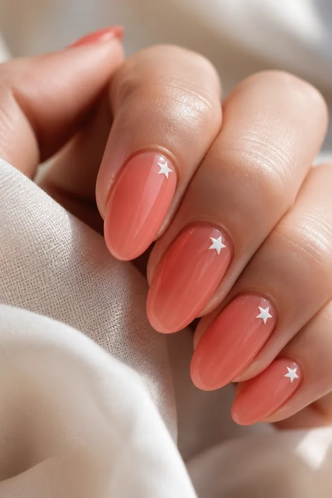 Glossy sheer coral almond nails with a tiny white five-point star on the side of the upper third; clean negative space otherwise.