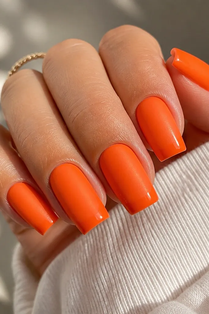 Square nails in a bright tangerine orange. The finish is satin-matte on the nail surface but the very edge and top coat look extra glossy, giving a two-texture effect.