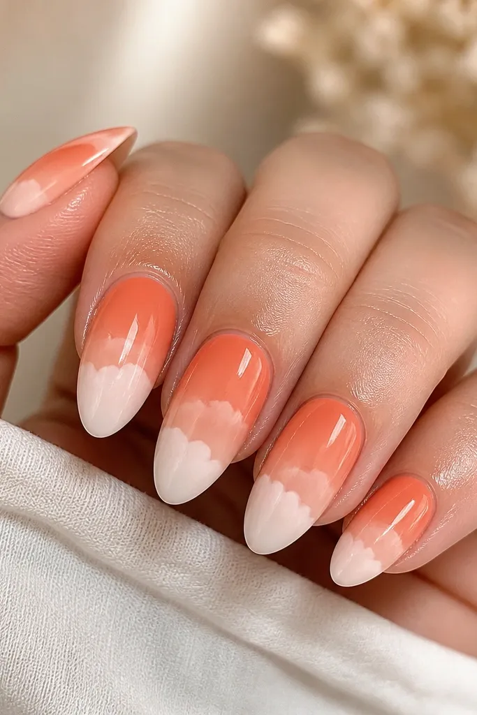 Five almond nails with a peach-to-coral sunrise fade from cuticle to mid-nail, then soft white cloud tips that look airbrushed and rounded, finished with a glossy top coat.