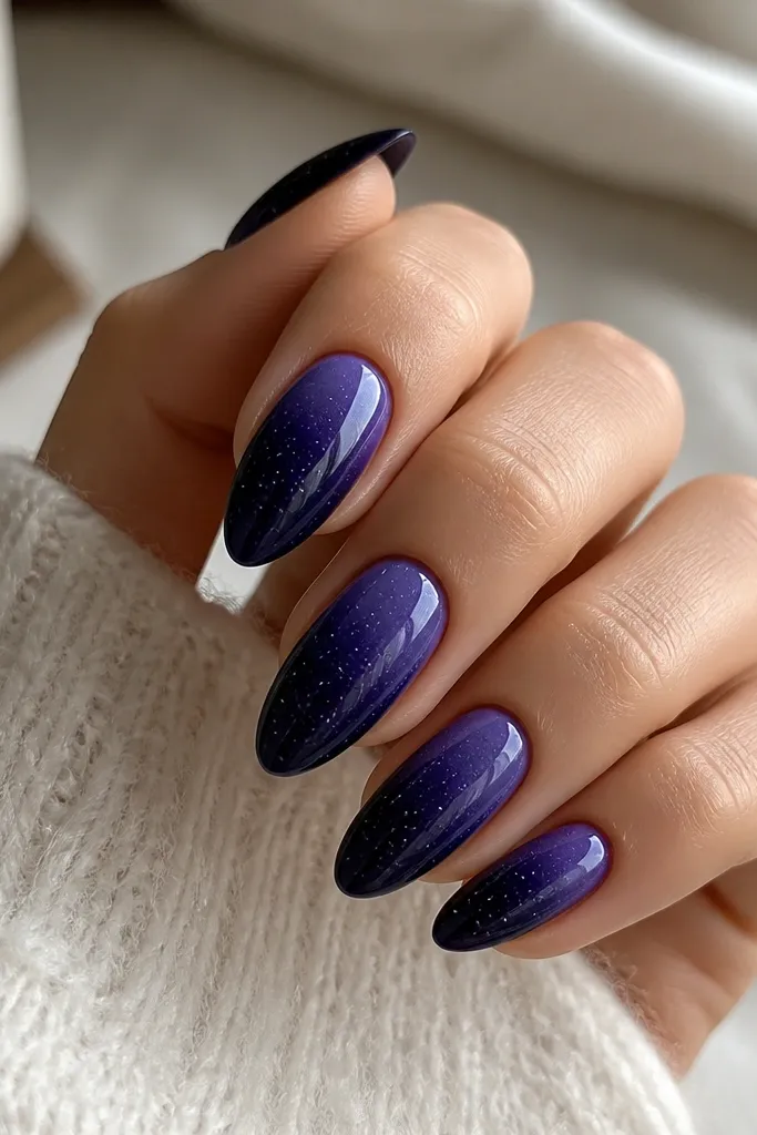 Almond nails with a deep blue-purple fade toward the tip, finished with tiny silver speckles scattered across the surface, glossy top coat.
