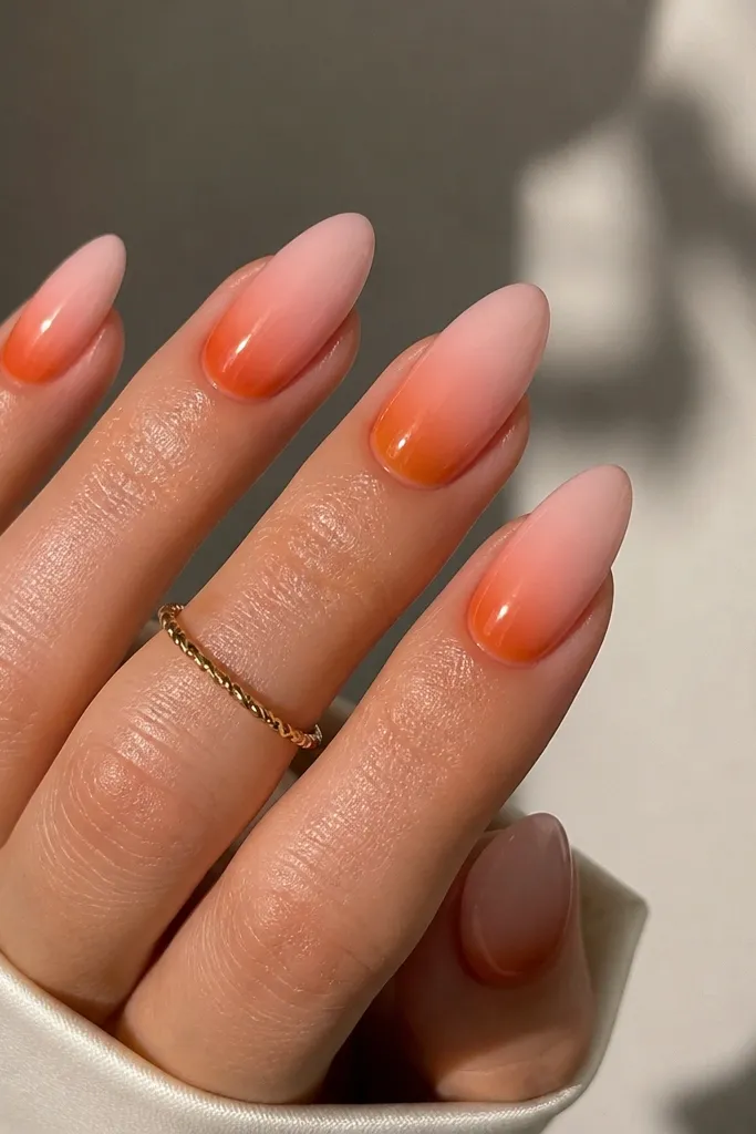 Almond nails with a soft pink base and a translucent orange glaze concentrated at the cuticle area, fading outward, glossy finish.