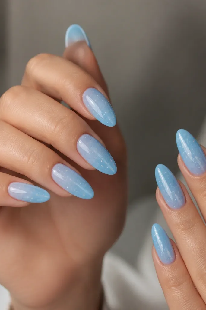 Almond nails with a sky blue gradient from cuticle to tip, and tiny white star specks scattered across the nails, glossy finish.