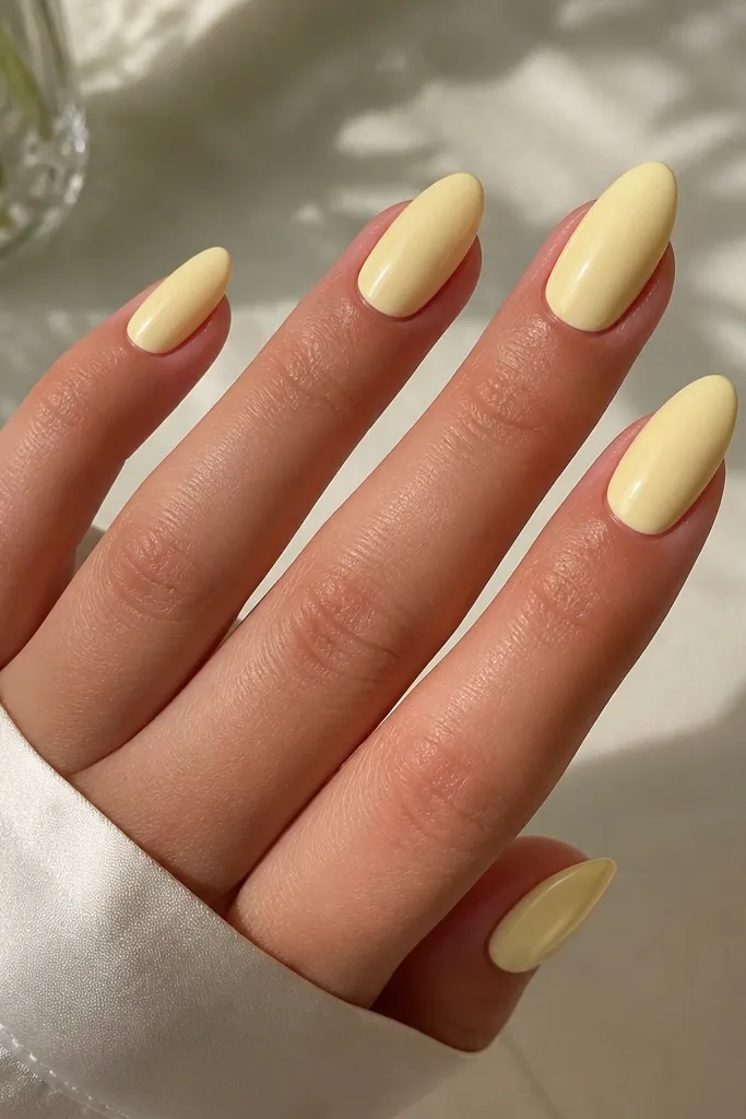Almond nails painted a creamy butter yellow that is opaque and smooth. The color looks slightly milky rather than neon. The cuticles are neat and the finish is glossy.