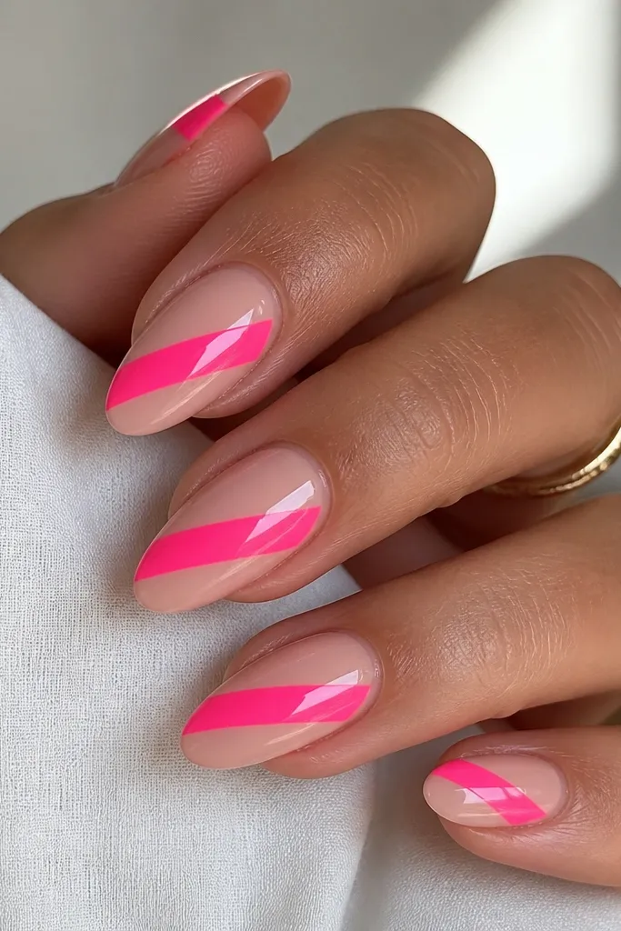 Almond nails with a nude base. A neon pink diagonal band cuts across the nail from lower left to upper right. The neon is opaque and glossy, with sharp edges.