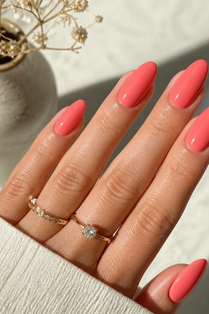 Almond nails painted a coral pink solid color with a smooth gel-like shine. The color is even from cuticle to tip with no streaks.