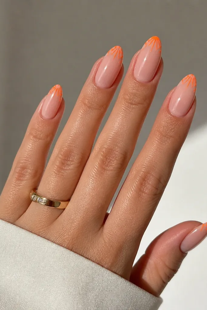 Almond nails with a nude base and neon orange lines radiating like tiny sunbursts only at the very tips. The lines are thin and crisp, with glossy shine.