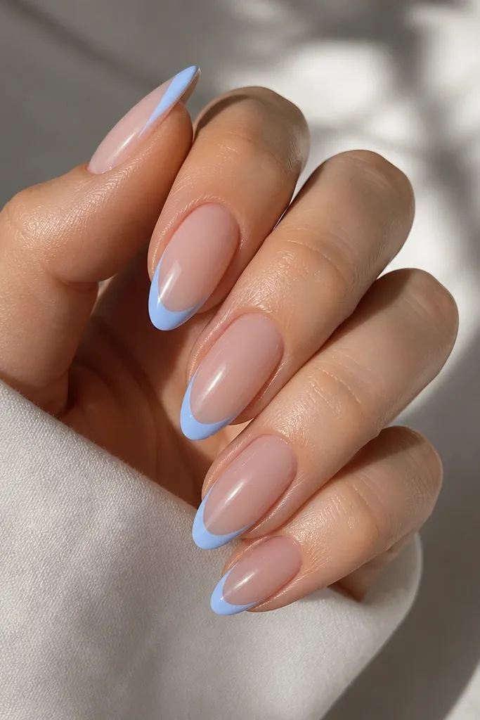Almond nails with a thin sky-blue smile line along the tip and a clear nude center; ultra-glossy, minimal look.