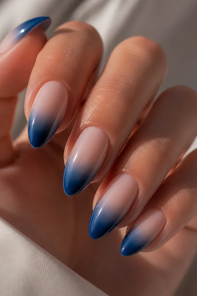 Almond nails with nude base fading into deep ocean blue at the tips; smooth ombre with glossy finish.