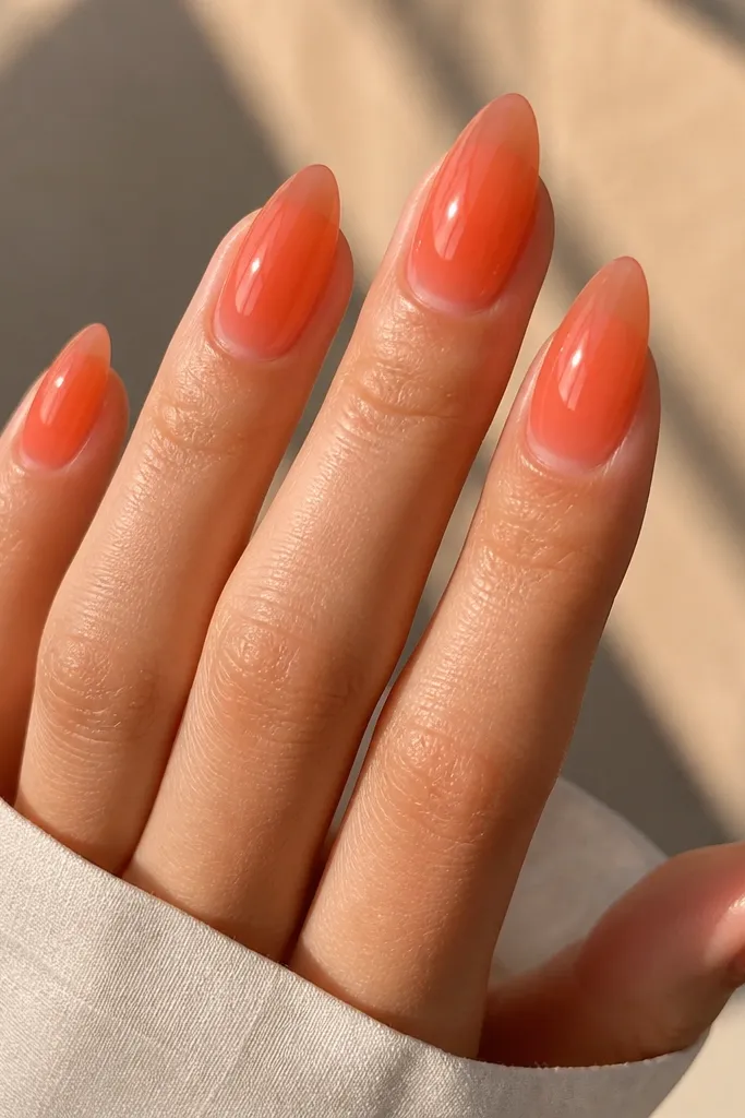 Almond nails in a translucent coral jelly color. The color looks layered, with the center slightly brighter and the edges more sheer. Everything is glossy, reflecting sunlight.