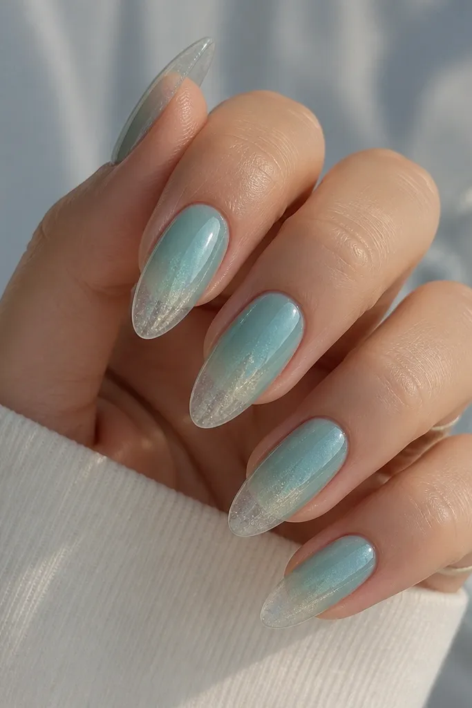 Almond nails with a soft sea-glass base in blue-green. Near the tips there is a translucent, almost clear zone like a frosted edge. Fine shimmer is visible under the gloss, especially toward the tips.