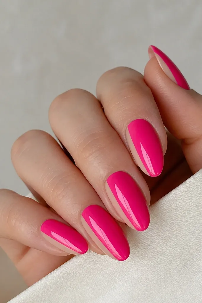 Almond nails painted hot pink glossy. On each nail, there is a narrow vertical negative space strip on one side, leaving bare nail. The negative strip is straight and clean, with a crisp line.
