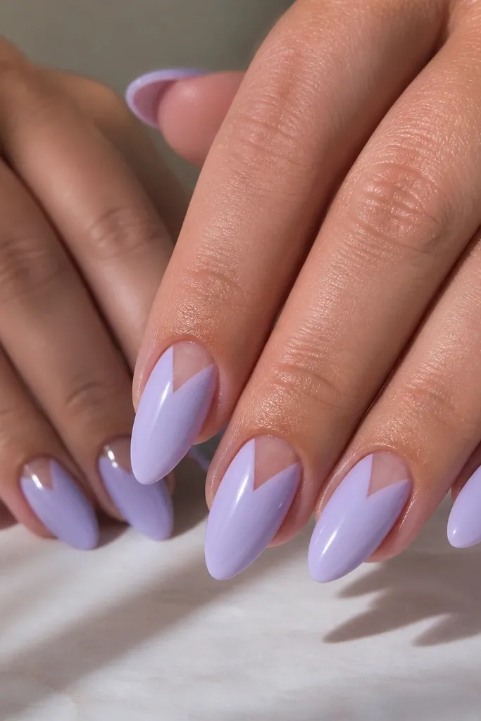 Almond nails with an iced lilac glossy base. At the cuticle, a clear negative-space V shape points toward the center of the nail. The V is crisp and symmetrical, leaving bare nail or clear gel.
