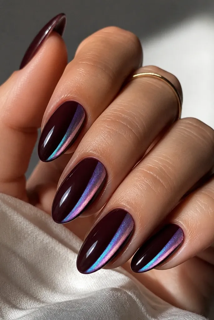 Almond nails painted deep black cherry glossy. On each nail, there is an opal chrome swipe along one sidewall, angled slightly toward the tip. The chrome shifts from pale pink to icy blue depending on light.