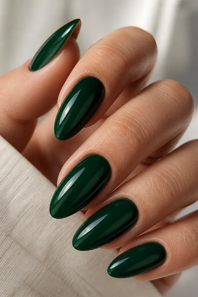 Almond nails in a deep emerald glossy color. The center of each nail looks slightly more domed and glass-like, with light reflecting in a smooth curve. No art besides the shine.