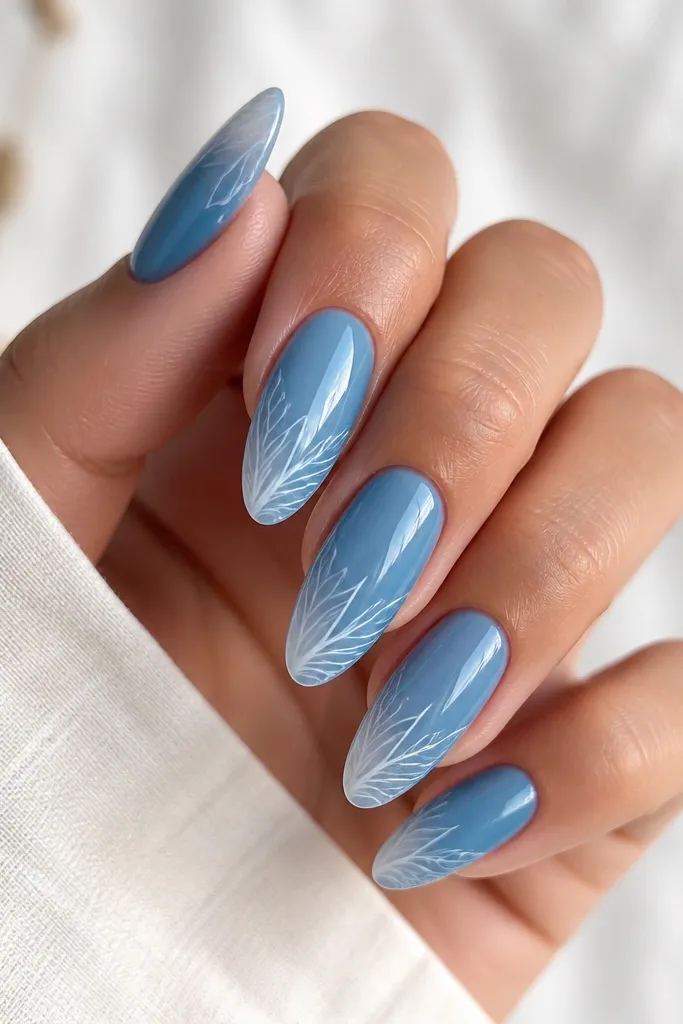 Ocean blue almond nails with a glossy finish. Each nail has a semi-transparent white overlay near the tip that looks like leaf veins, branching out in thin lines toward the center.
