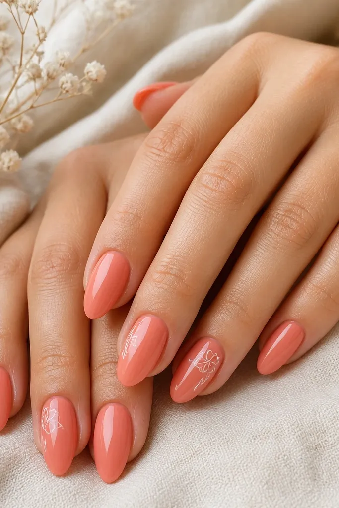 Coral almond nails with a glossy finish. On the accent nails there is a small white flower drawn near the cuticle and a tiny fern line beside it, both in thin strokes.