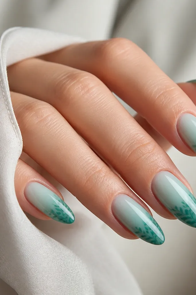 Turquoise jelly almond nails. The base is lighter near the cuticle and deeper at the tip, and on the tip area there are tiny leaf silhouettes stamped or painted in darker green.