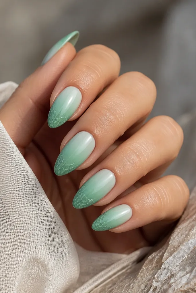 Almond nails with seafoam ombre - light seafoam near the cuticle fading into deeper green at the tip. On each nail, the tip has a thin leaf pattern like skin texture, drawn in darker green lines.