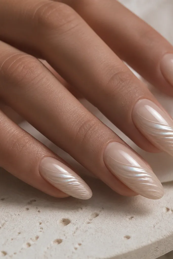 Almond nails with sandstone nude base, a single sweeping pearl chrome wave across the center, and fine shell-like ridges etched lightly.