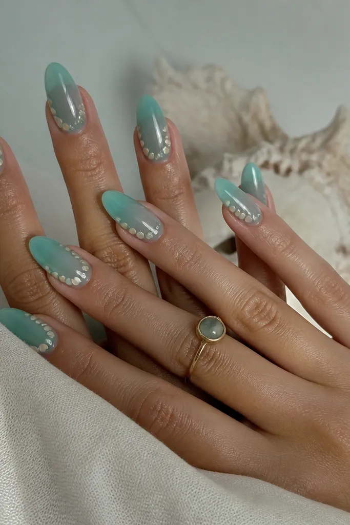 Medium almond nails in sea glass teal with a clear jelly top, scattered pearl shell dots near the cuticle and along the sides, glossy.