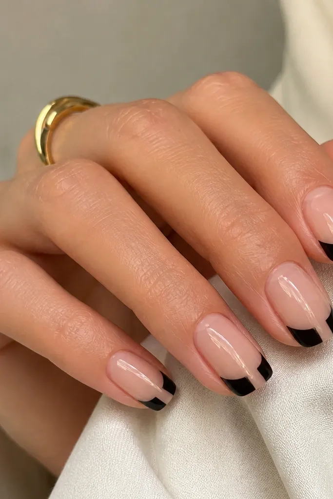 Nude glossy nails with a crisp black geometric tip that covers the outer third, plus a small negative-space notch in the center of the tip.