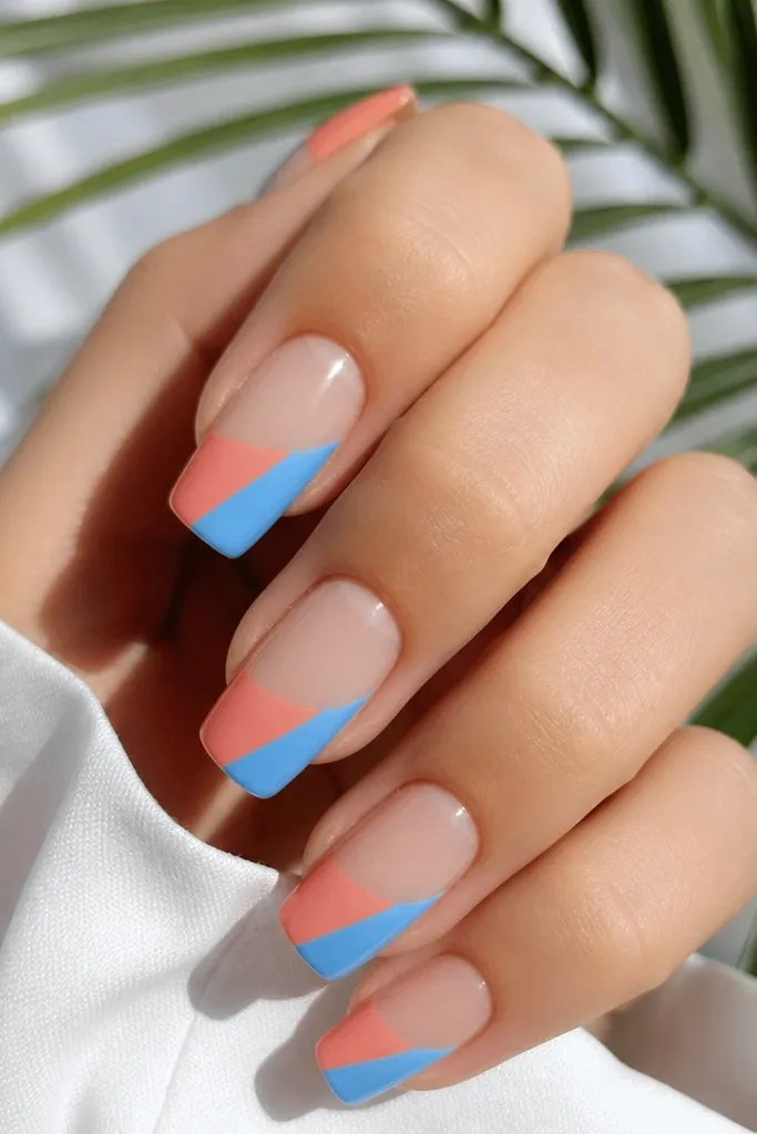 Two-tone split nails with a diagonal divide between coral and sky blue on glossy square tips; base is clear and the split stops before the cuticle.